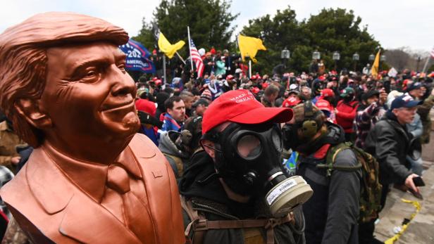 (FILES) A supporter of US President Donald Trump wears a gas mask and holds a bust of him after he and hundreds of others stormed stormed the Capitol building on January 6, 2021 in Washington, DC. Donald Trump hits the campaign trail in the first-in-the-nation presidential nominating state of Iowa on January 6, 2024 as Americans mark the third anniversary of the deadly assault on the US Capitol by a mob of his supporters. People watched in horror on January 6, 2021, as TV images were beamed into homes nationwide showing rioters -- egged on by the ex-president and fueled by his false claims of voter fraud -- storming the seat of US democracy to halt the transfer of power. (Photo by ROBERTO SCHMIDT / AFP)