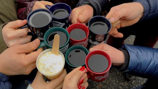 Mehrere Personen stoßen mit Tassen mit Glühwein und einem Getränk mit Sahne an.