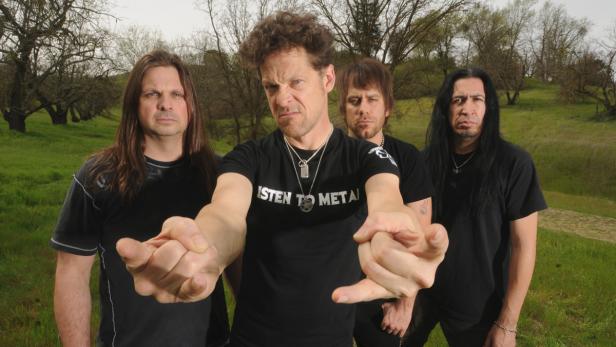 Eine Metal-Band posiert vor einer grünen Hügellandschaft für ein Foto.