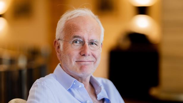 Ein älterer Mann mit Brille und hellblauem Hemd lächelt in die Kamera.