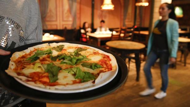 Ein Kellner serviert eine Pizza mit grünem Salat in einem Restaurant.