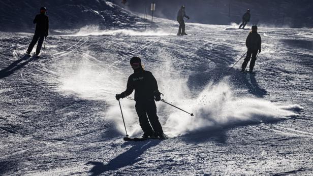 Skifahrer auf einer Skipiste mit aufgewirbeltem Schnee.