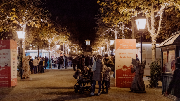 Eine beleuchtete Allee mit Weihnachtsmarktständen und Besucher:innen.