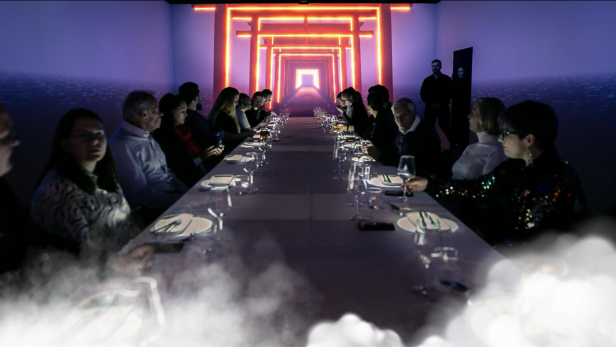 Gäste sitzen an einem langen Tisch vor einem beleuchteten Torii-Tunnel.