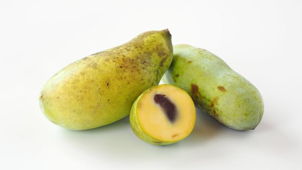 Zwei ganze Indianerbananen und eine halbe Frucht liegen auf einem weißen Untergrund.