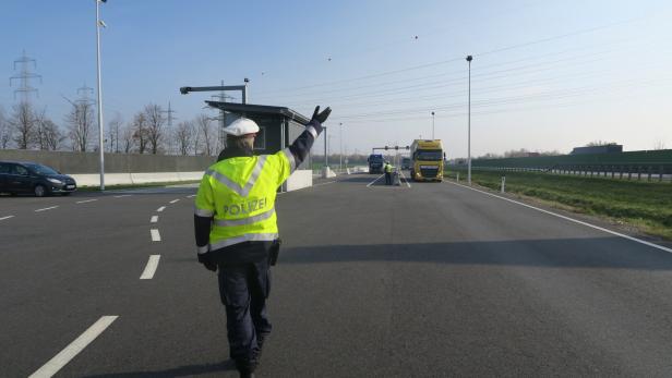 Ein Polizist in gelber Jacke winkt Lastwagen auf einer Autobahn durch eine Kontrollstelle.