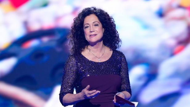 Eine Frau mit lockigem Haar in einem lila Kleid hält eine Rede.