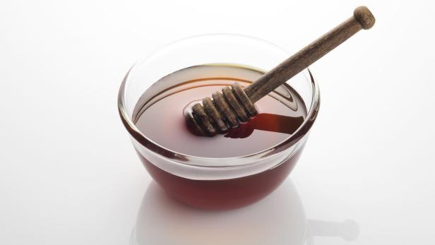 Eine Glasschale mit Honig und einem hölzernen Honiglöffel.