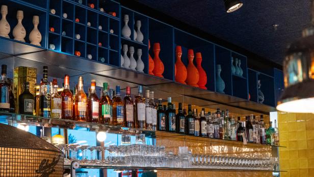 Eine Bar mit Spirituosenflaschen und dekorativen Vasen in Regalen.