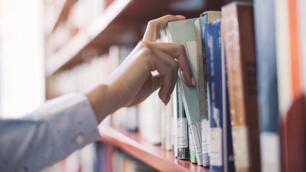 Frau nimmt sich ein Buch aus dem Regal