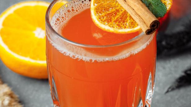 Ein Glas mit einem orangefarbenen Getränk, garniert mit Orange, Zimtstange und Minze.