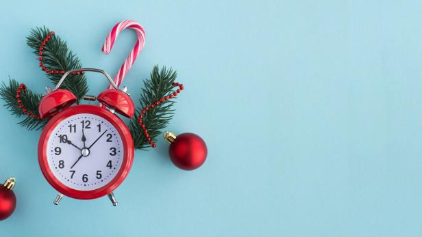 Ein roter Wecker mit Tannenzweigen, Christbaumkugeln und Zuckerstange auf blauem Hintergrund.