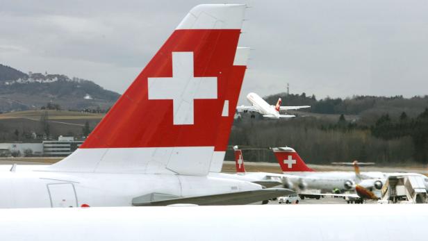 Schweizer Flugzeuge am Flughafen, ein Flieger startet im Hintergrund.