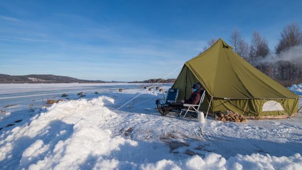 Mann sitzt vor einem Zelt im Schnee