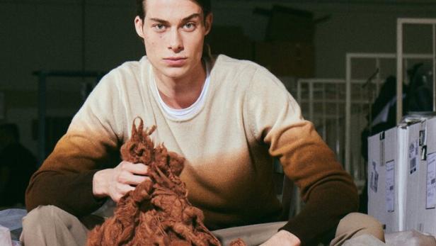 Ein Mann sitzt inmitten von Säcken mit farbiger Wolle.