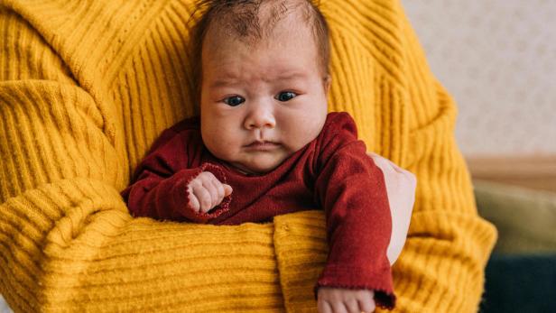 Baby auf dem Arm einer Frau, die einen gelben Pulli trägt