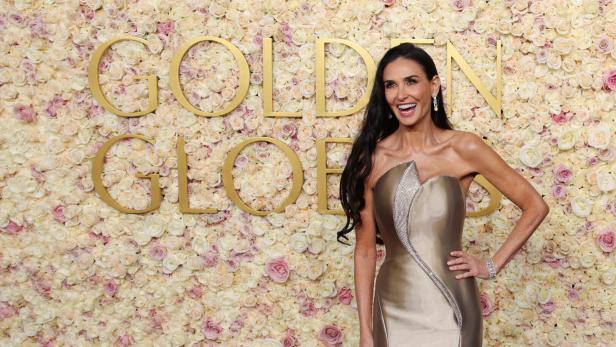 Demi Moore posiert auf dem roten Teppich vor einer Wand aus Rosen bei den Golden Globes.