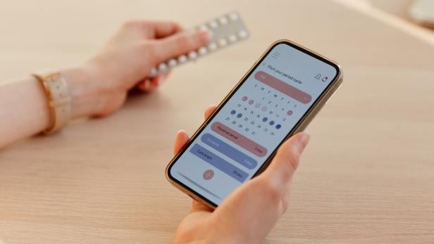 Frau hält Handy und nutzt Zyklus-App.