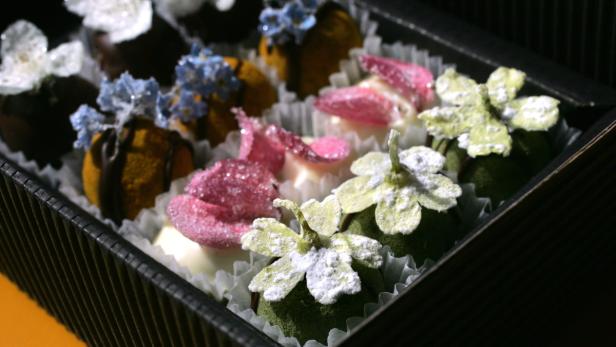 Eine Schachtel Pralinen, verziert mit Zuckerblüten und Blütenblättern.