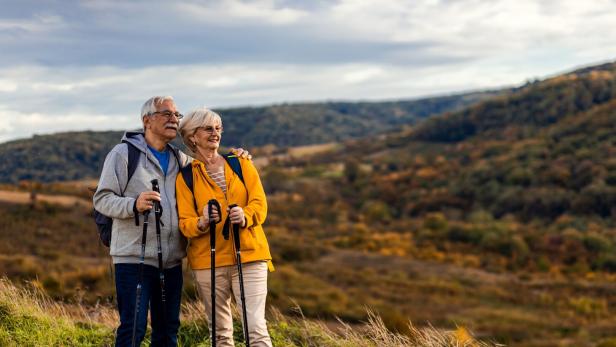 Ein älteres Paar wandert mit Stöcken in einer hügeligen Landschaft.