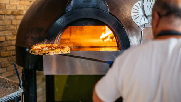 Ein Mann schiebt eine Pizza in einen Ofen.