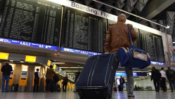 Ein Reisender mit Gepäck vor einer Anzeigetafel auf einem Flughafen.