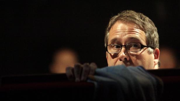 Ein Mann mit Brille schaut aufmerksam hinter einer Barriere hervor.