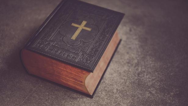 Die Bibel mit goldenem Kreuz-Aufdruck liegt auf einem Steinboden