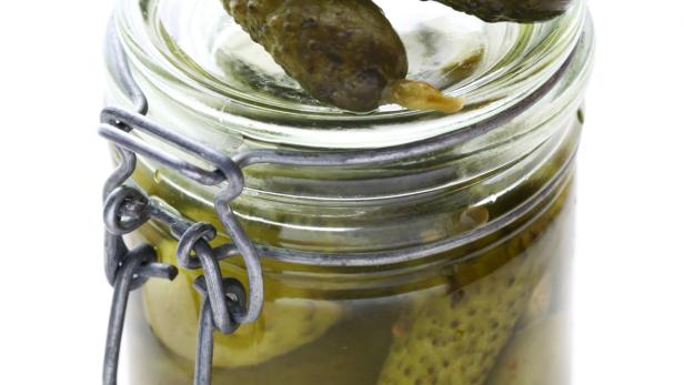 Ein Glas mit eingelegten Gurken, zwei davon liegen obenauf.