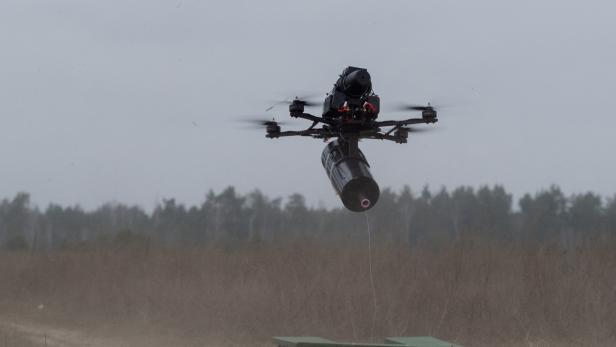 Eine Drohne trägt eine zylindrische Last unter sich.