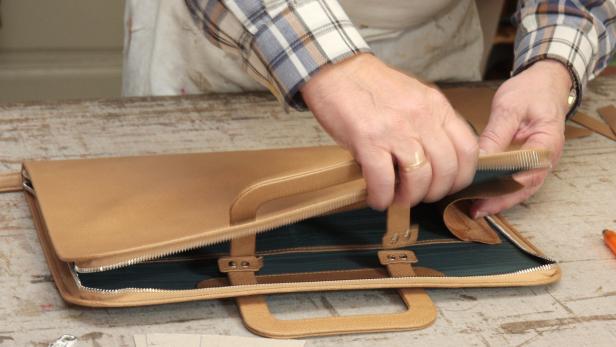 Ein Handwerker bearbeitet eine hellbraune Ledertasche mit einem Werkzeug.