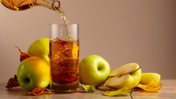 Apfelsaft wird in ein Glas gegossen, umgeben von Äpfeln.