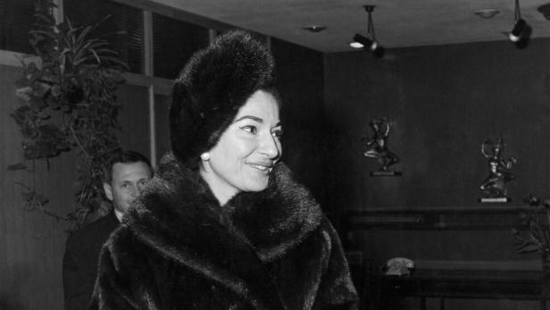 Maria Callas in einem Pelzmantel und einer Pelzmütze, die eine Handtasche und eine Brille hält.