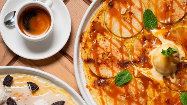 Zwei Teller mit Crêpes, garniert mit Äpfeln, Oreo-Keksen und Kokosraspeln, dazu Kaffee.