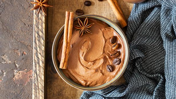 Eine Schüssel mit Schokoladenmousse, garniert mit Kaffeebohnen, Zimtstangen und Sternanis.
