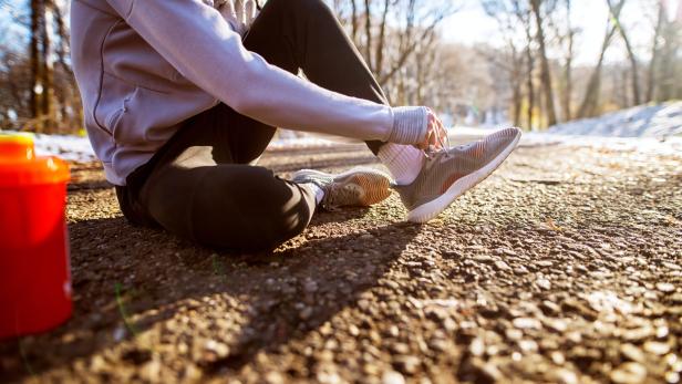 Mann schnürt sich vor ihrem 10.000-Schritte-Spaziergang die Schuhe.
