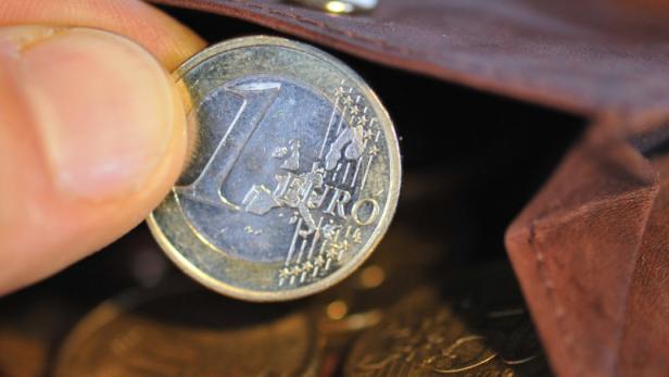 Eine Hand legt eine 1-Euro-Münze in ein braunes Lederportemonnaie.