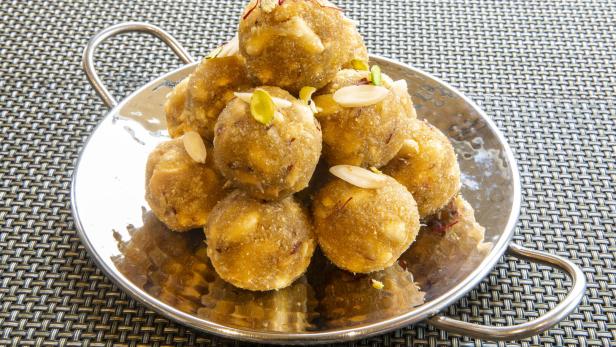Eine silberne Schale ist gefüllt mit indischen Süßigkeiten, die mit Mandeln und Pistazien garniert sind.