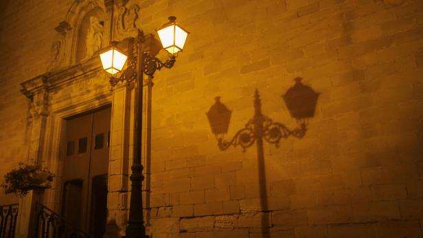 Eine beleuchtete Straßenlaterne vor einer Kirche bei Nacht.