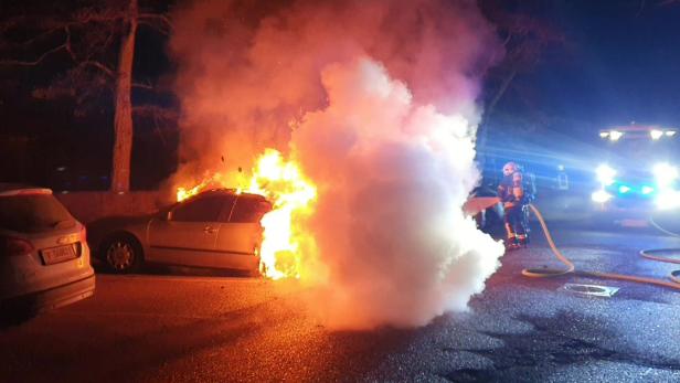 Ein Feuerwehreinsatz, bei dem ein brennendes Auto gelöscht wird und im Hintergrund ist das Feuerwehrauto