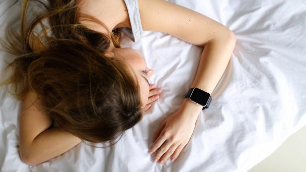 eine Frau liegt schlafend mit einer Smartwatch am Handgelenk im Bett