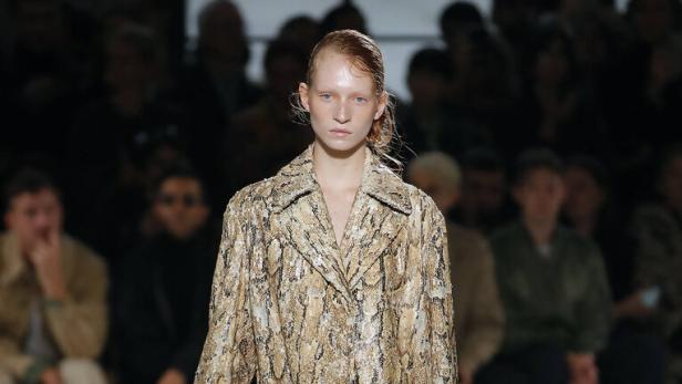 Ein Model auf dem Laufsteg trägt einen Mantel mit Schlangenmuster und rote Schuhe.