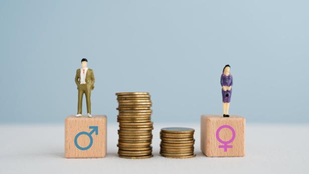 Gender pay equality concept. Miniature of man and woman on wooden cube block with stack of coins