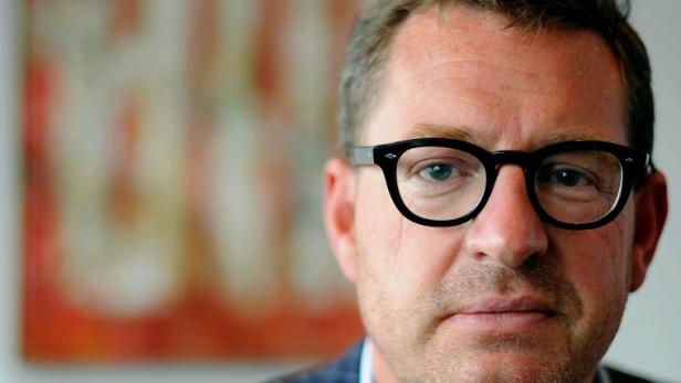Ein Mann mit Brille und Anzug vor einem unscharfen Hintergrund.