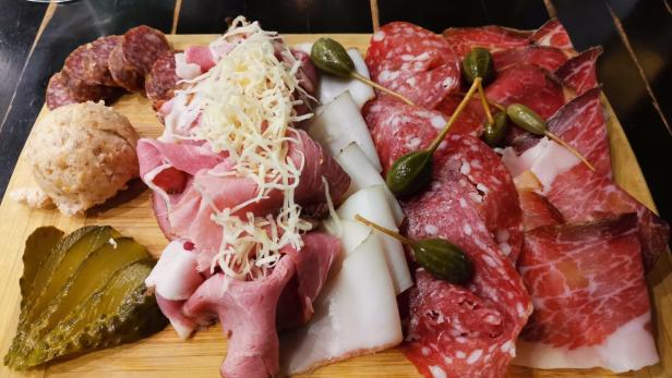 Eine Platte mit Wurst, Schinken, Speck, Griebenwurst, Gewürzgurken und Kapernäpfeln.