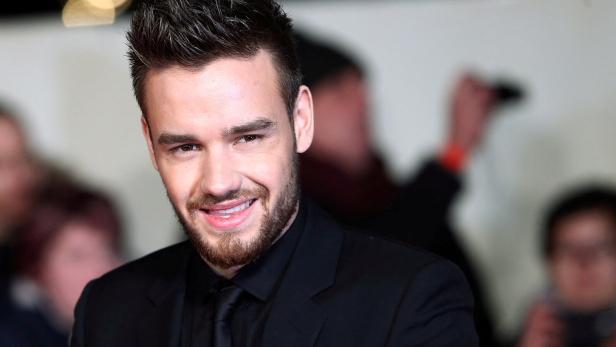 Liam Payne lächelt in einem schwarzen Anzug.