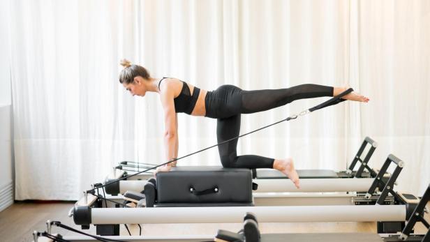 Eine Frau trainiert auf einem Reformer-Pilates-Gerät.