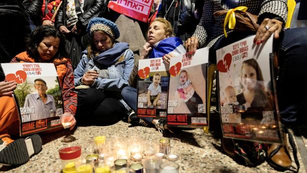 Menschen sitzen mit Schildern und Kerzen, die zur Freilassung von Geiseln aufrufen.