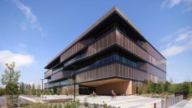 Zwei Personen fahren mit Fahrrädern vor einem modernen Bürogebäude.