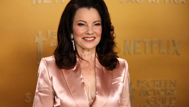 Fran Drescher trägt einen rosa Blazer vor einem goldenen Hintergrund.
